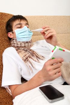 Sick Teenager in Flu Mask with pack of pills on the Sofa at the Home