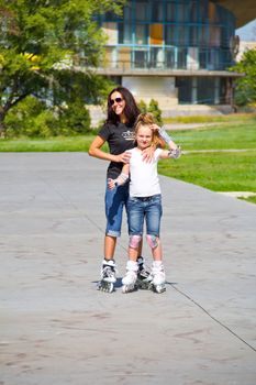 Learning mother and daughter on roller skates in summer