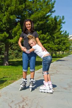 Learning mother and daughter on roller skates in summer