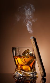 Glass of whiskey and cigar on brown background
