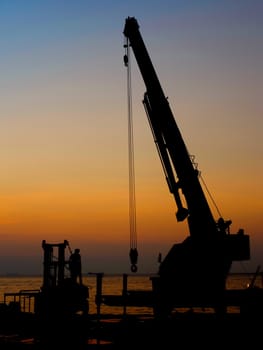 Silhouette crane working at port with sunset sky background