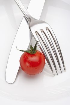 cherry tomato on a plate with fork and knife isolated on white