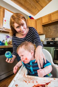 Grumpy baby in kitchen is being fed from her bottle