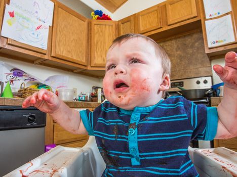 Grumpy baby in kitchen is covered with food