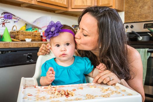 Woman in a messy kitchen kisses her baby