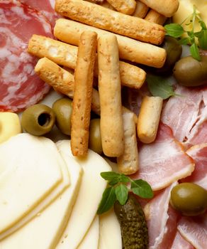 Background of Delicious Smoked Meat and Smoked Salami Salchichon with Bread Sticks, Cheese Sauce, Green Olives , Emmental Cheese and Gherkins closeup