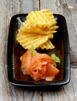 Delicious Smoked Salmon with Rifled Potato Chips on Black Plate isolated on Rustic Wooden background