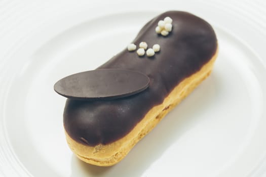 Single chocolate eclair with space for text on white  plate. Warm colors. Shallow dof. 