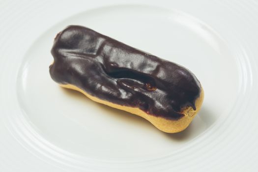 Single chocolate eclair on white  plate. Warm colors. Shallow dof. 