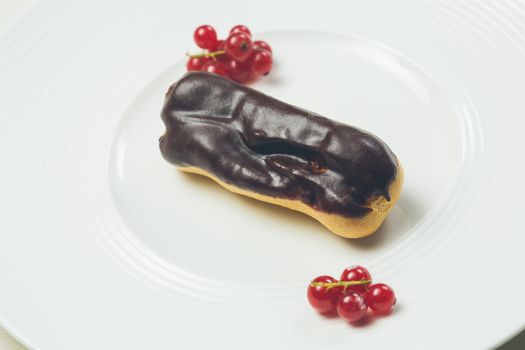 Single chocolate eclair on white  plate. Warm colors. Shallow dof. 