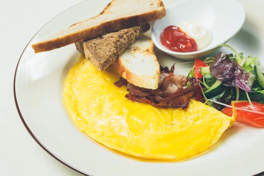 Omelet with bacon served on white plate, vegetables aside. Warm colors. Shallow dof. 