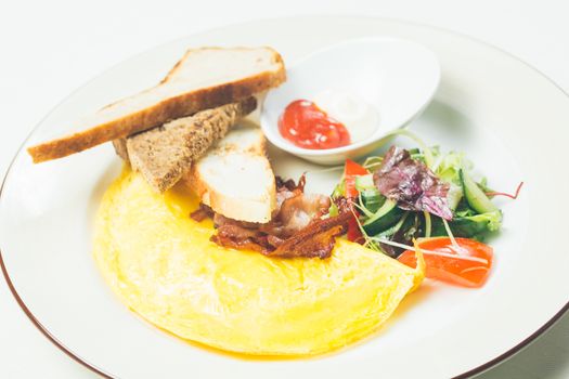 Omelet with bacon served on white plate, vegetables aside. Warm colors. Shallow dof. 
