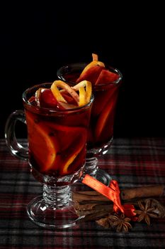 Hot red mulled wine with fruits and cinnamon on checkered tablecloth