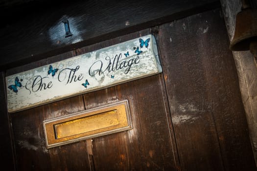 A weathered and textured front door with a sign saying "One The Village".