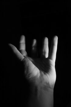 A low key photo of an open hand with upstretched fingers.