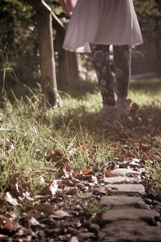 The edge of a path leads towards the legs of a child taking a stroll on an autumn day.