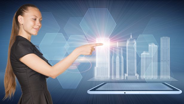 Beautiful businesswoman watching as her forefinger touches spatial layouts of buildings, generating rays of light in the point of contact. Tablet PC below layouts, hexahegons as backdrop.