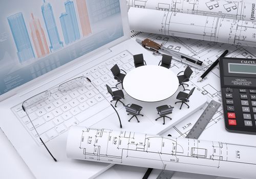 Miniature round table with chairs scrolled drawing and glasses on laptop keyboard, calculator and a few other tools on spread architectural drawings, couple of scrolled drawings beside. Concept of construction business.