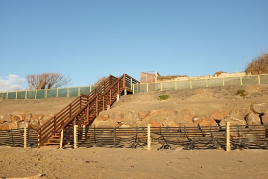 A set of wooden stairs, steps, built over a constructed dune with sand drift fence, base rock and overlayed sand.