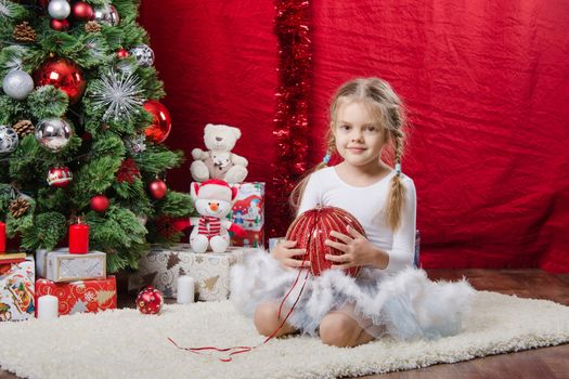 Girl sitting on a rug in the Christmas tree with Christmas tree balls
