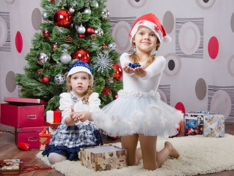 Two girls sitting on a rug in a Christmas tree with gifts