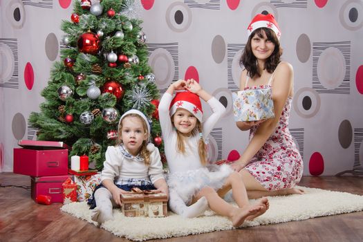 Mom and two daughters sitting on a rug in the Christmas tree