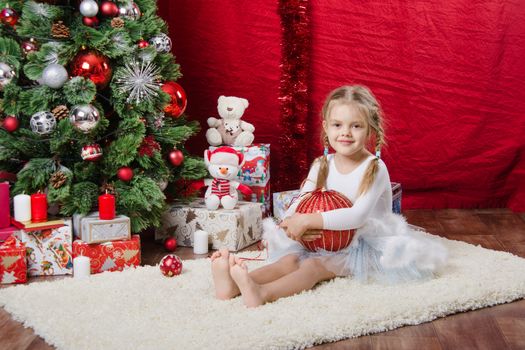 Girl sitting on a rug in the Christmas tree with Christmas tree balls