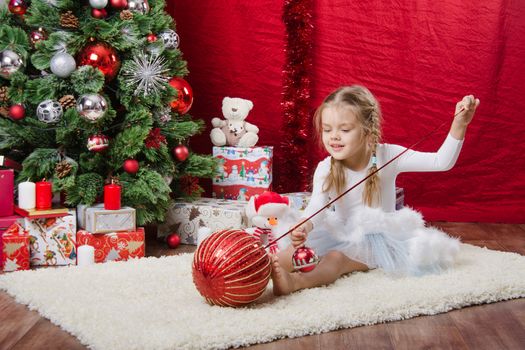 Girl sitting on a rug in the Christmas tree with Christmas tree balls