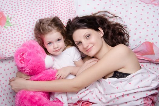 Mom and daughter with an excellent mood lie in bed