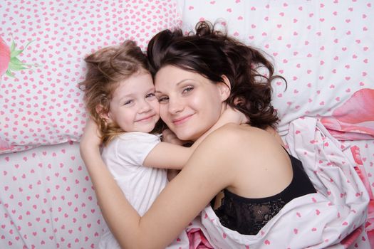 Mom and daughter with an excellent mood lie in bed