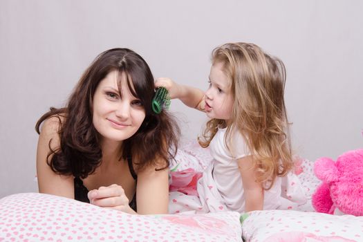 Daughter mother combing her hair lying in bed