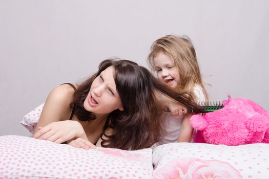 Daughter mother combing her hair lying in bed