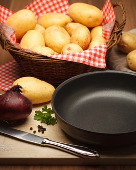 Fryingpan with potatoes an onion on wood