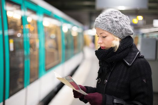 Casually dressed woman wearing winter coat, waiting on a platform for a train to arrive, orientating herself with public transport map. Urban transport.