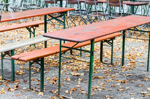 Autumn mood in a public beer garden. Chairs andl seat benches with foliage.