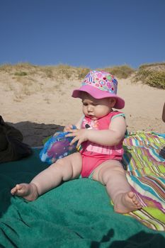 baby with pink hat sitting on green towel at beach