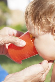 side face baby drinking from orange plastic cup