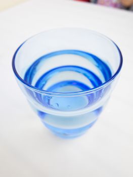 macro of blue glass with water on white tablecloth
