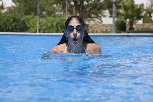 woman with goggles swimming breaststroke in a blue pool