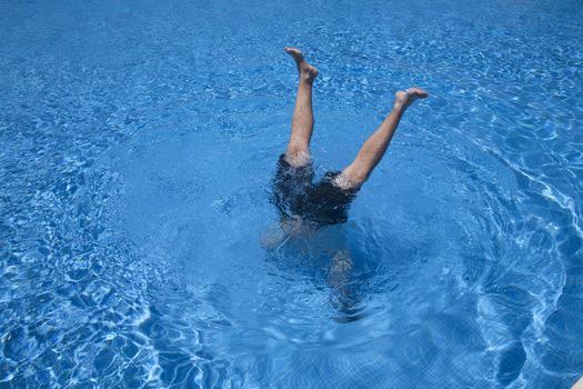 man handstands underwater with two legs peering in a blue pool