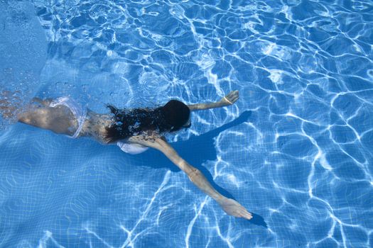 woman with white bikini swimming open arms in a blue pool