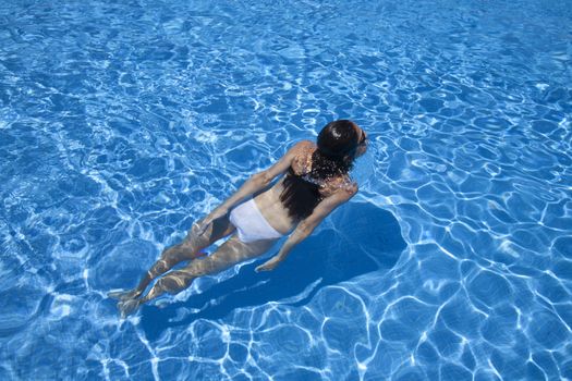 woman with white bikini sticking her head out of water in a blue pool