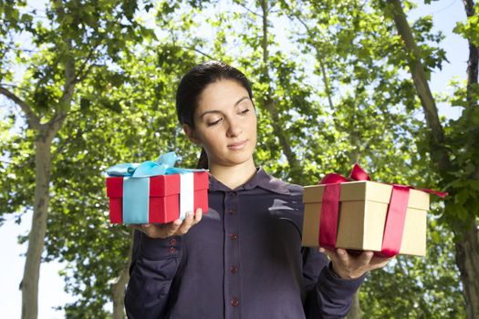pretty brunette woman with two gift boxes over green trees background
