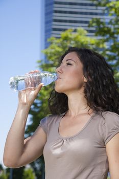 curly brunette woman drinking water from plastic bottle