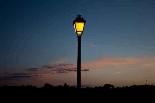 The streetlamp iluminates the country side, anticipating the coming night