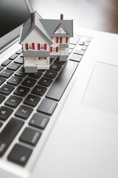 Miniature House And Laptop Computer Resting on Desktop.