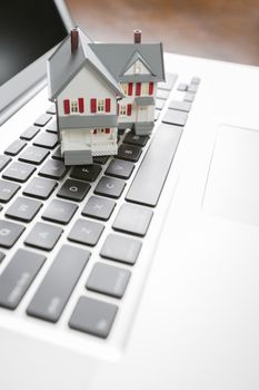 Miniature House And Laptop Computer Resting on Desktop.