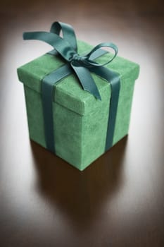 Green Gift Box with Ribbon and Bow Resting on Wood Surface.