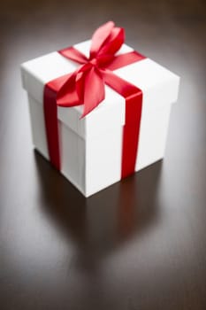 White Gift Box with Red Ribbon and Bow Resting on Wood Surface.