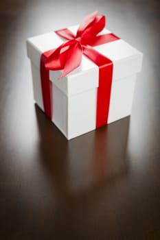 White Gift Box with Red Ribbon and Bow Resting on Wood Surface.